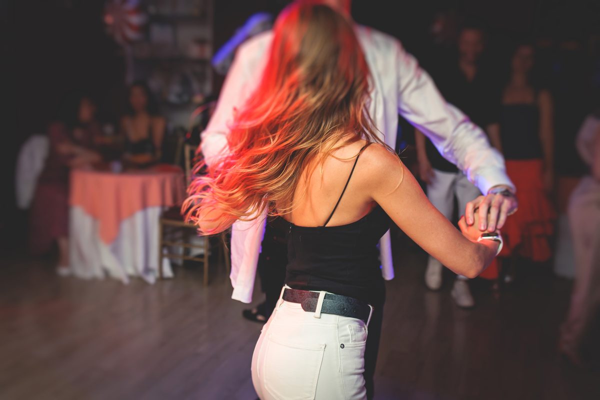 A couple dancing close at a nightclub, hands joined, against red leather booths